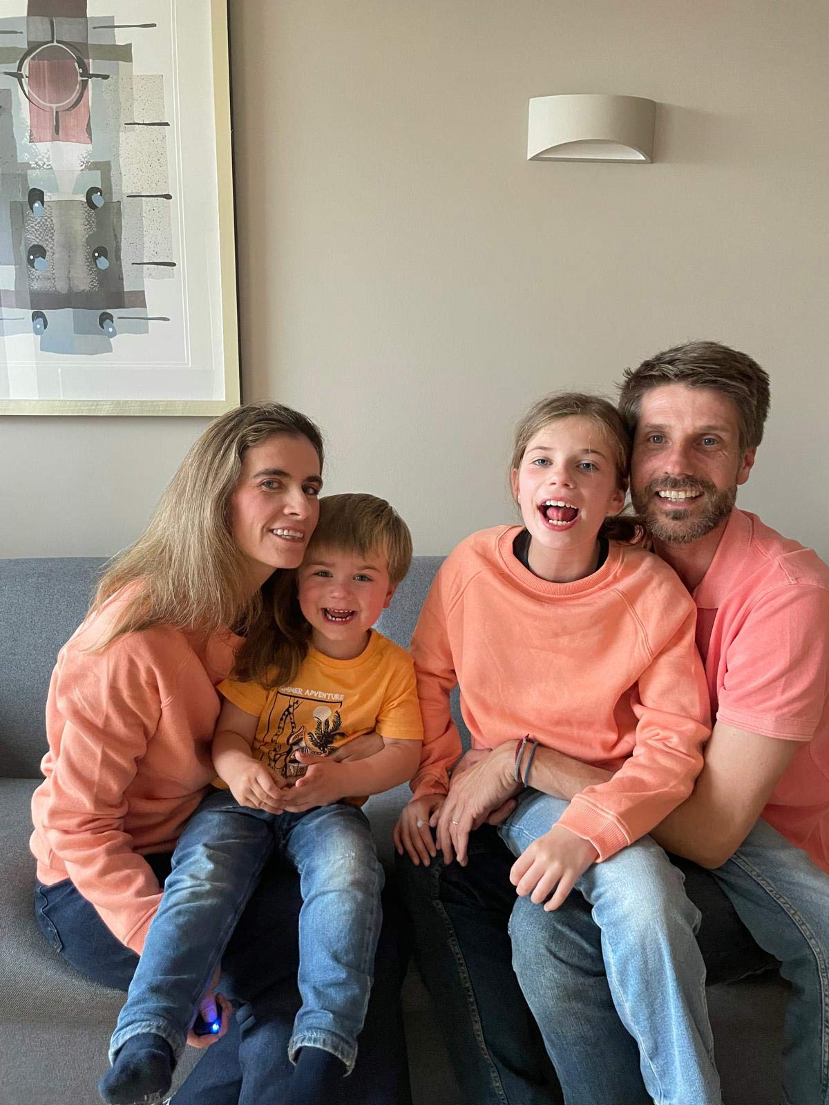 A smiling family of four pose together on a gray sofa.